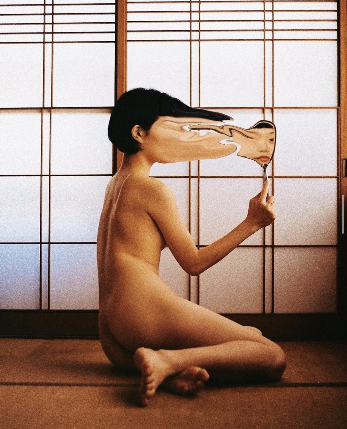 Editorial photograph of a seated figure holding a distorted mirror