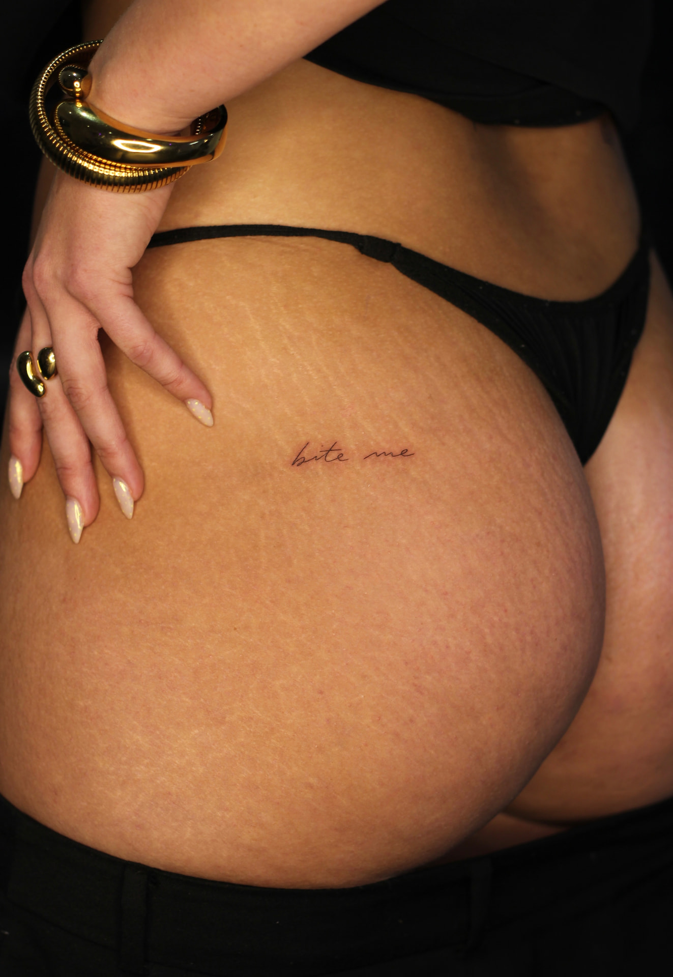 Fine line script tattoo reading bite me on the hip with gold jewellery