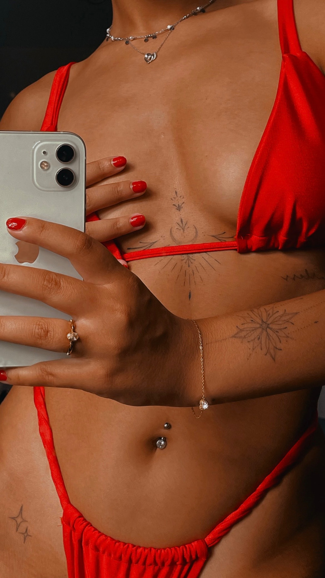 Mirror selfie in a red bikini showing fine line sternum and hand tattoos