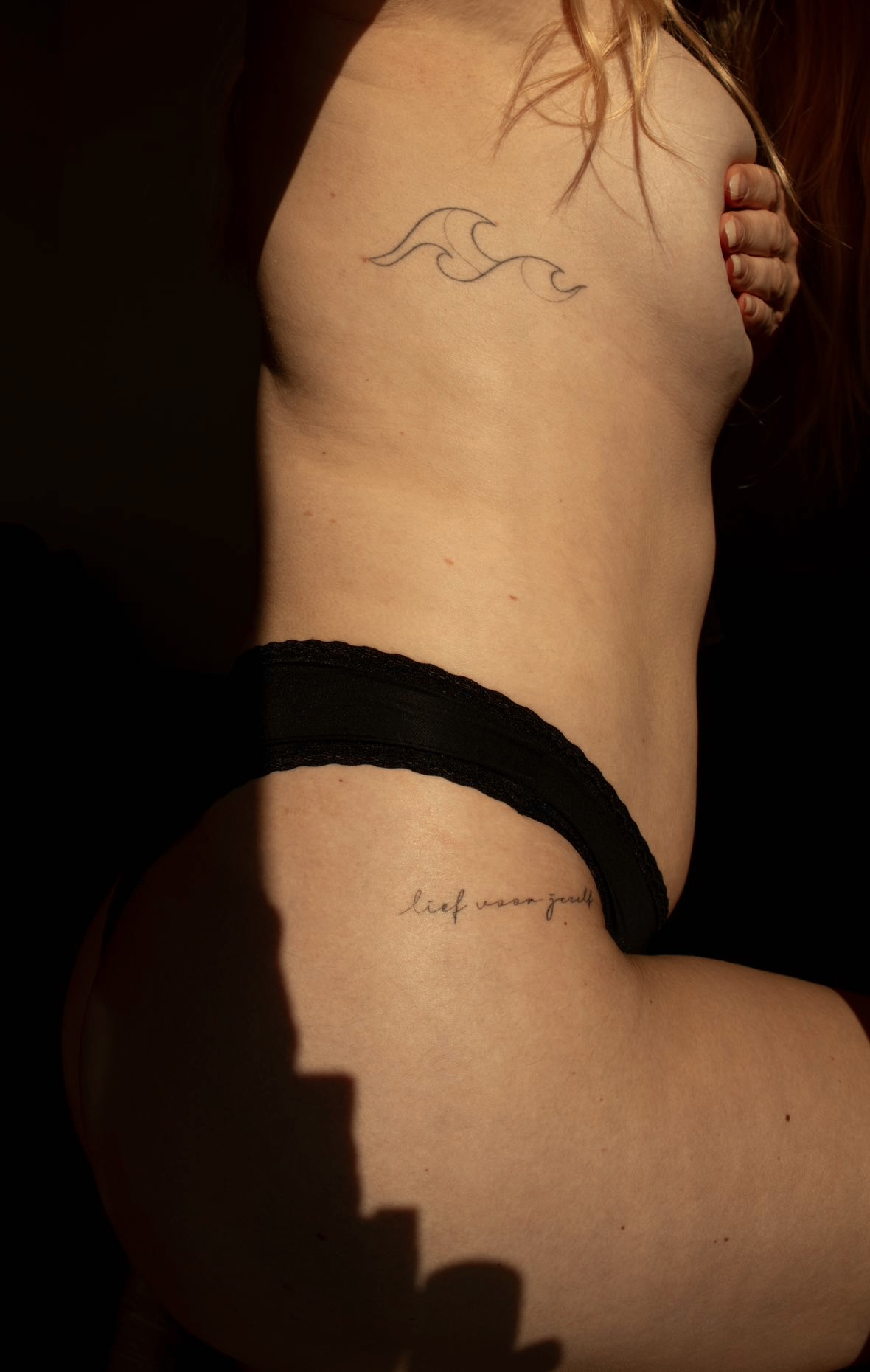 Fine line wave tattoo and script on a woman's side in warm daylight